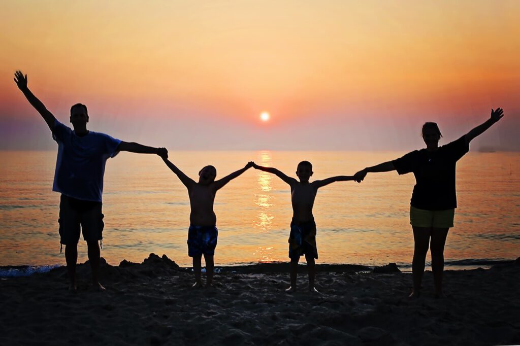 Mama, tata i dzieci trzymają się za ręce. Stoją na plaży podczas zachodu słońca